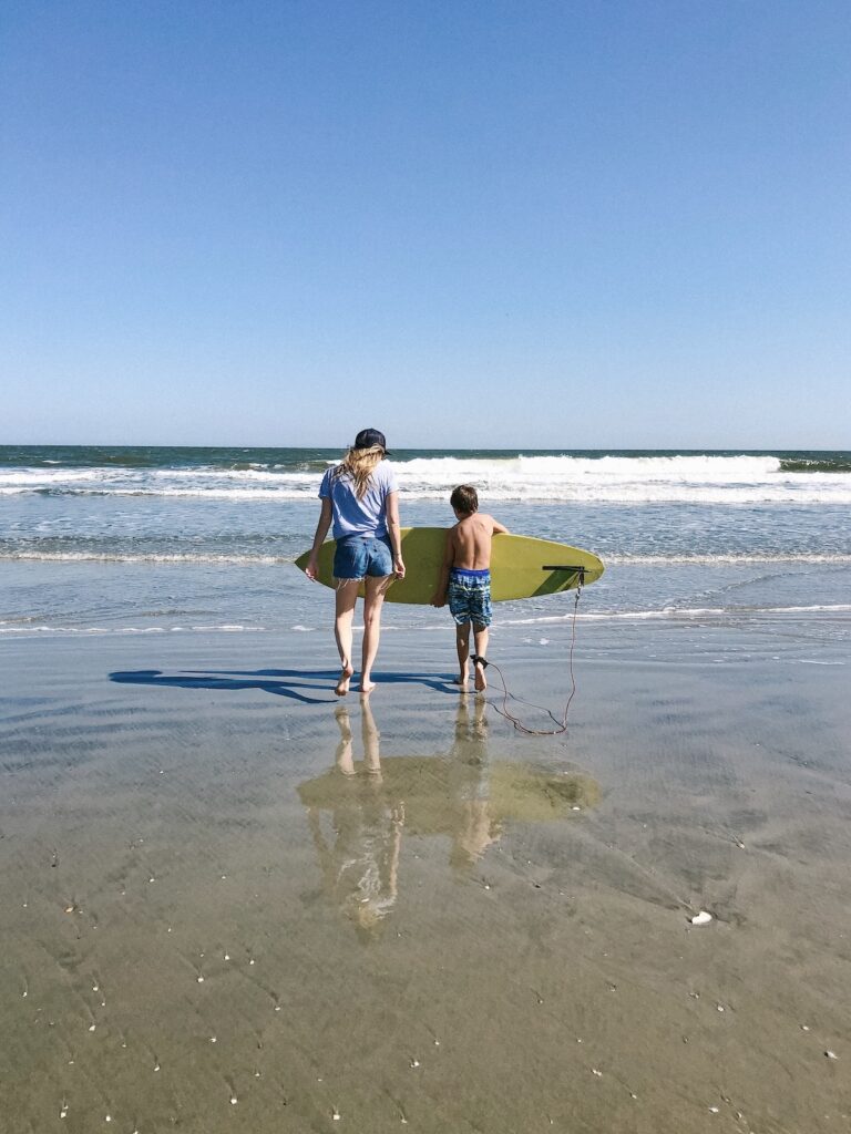 Woman and boy carrying a surf board into the ocean on Folly Beach, South Carolina. Folly is the best beach in Charleston for surfing.